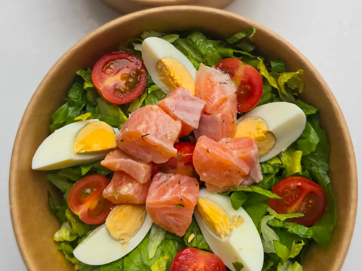 Almuerzo individual servido en envase de cartón: ensalada fresca con salmón, huevo y tomate